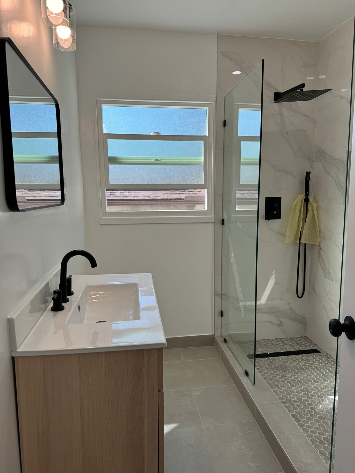 Bathroom with wood-tone vanity, frameless glass shower, marble-look tile and black fixtures