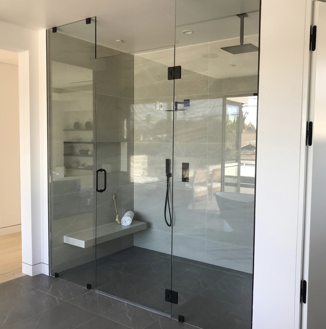 Walk-in shower with frameless glass, black fixtures, floating bench and recessed shelves