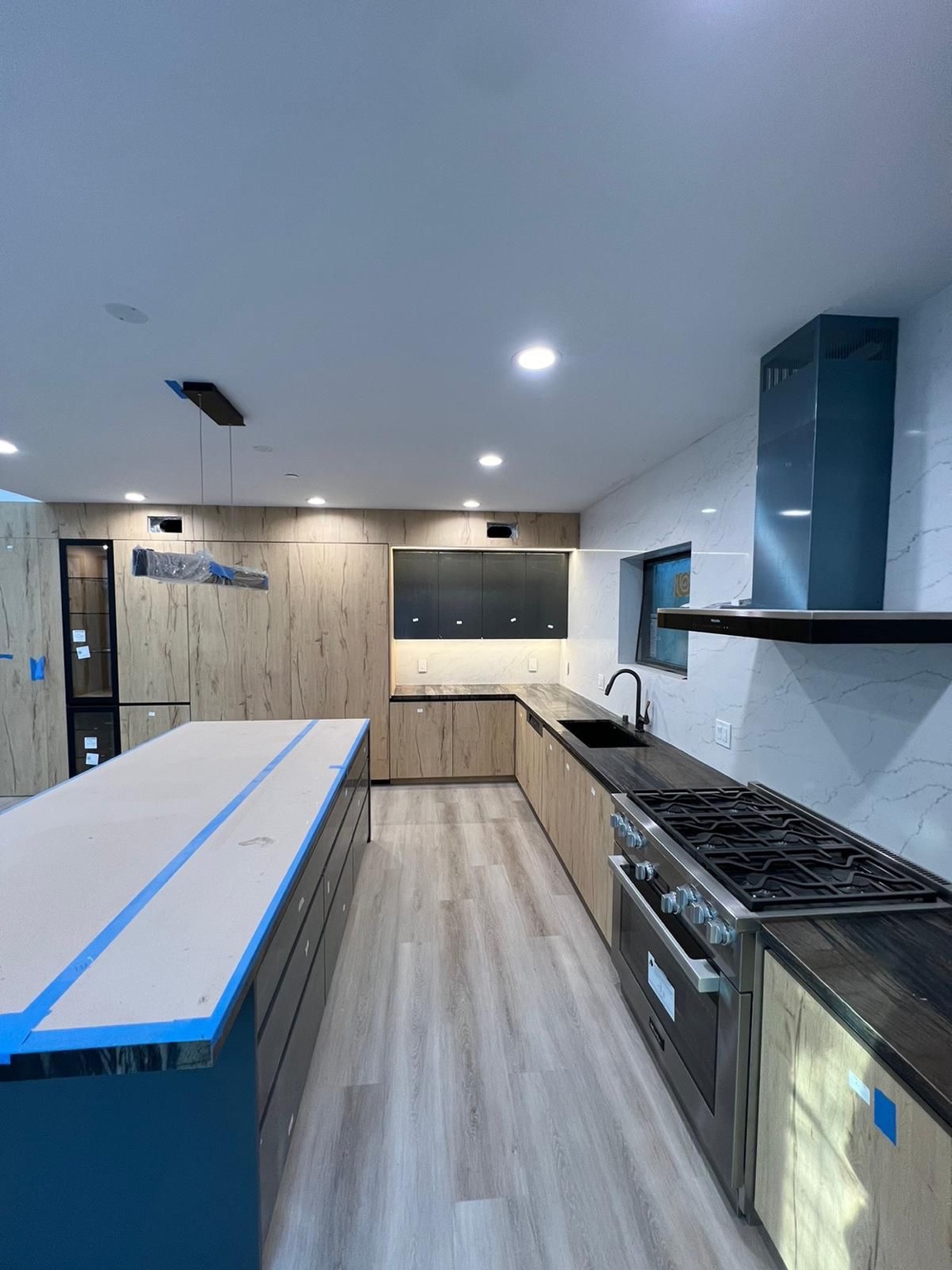 Kitchen in progress with wood-look cabinets, island, dark countertops and range hood