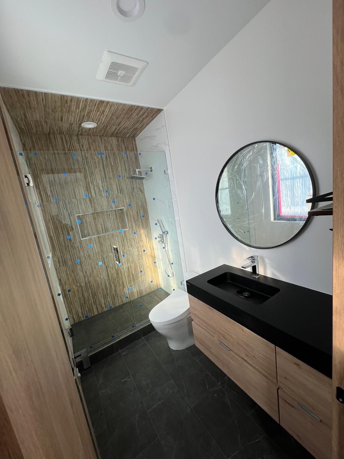 Bathroom in progress with wood-look shower tile, glass enclosure and round mirror